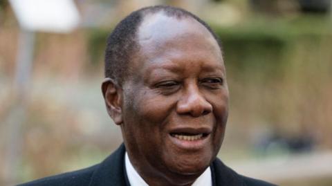 Alassane Ouattara smiles, wearing a dark jacket and a white shirt.