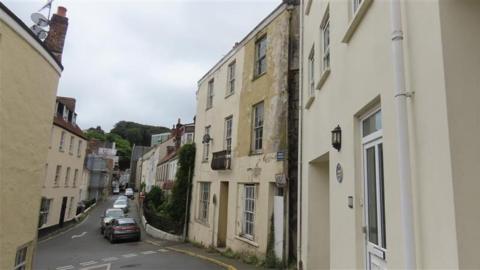 Houses on Mount Durand on the right. There is a road at the centre and there are parked cars. 