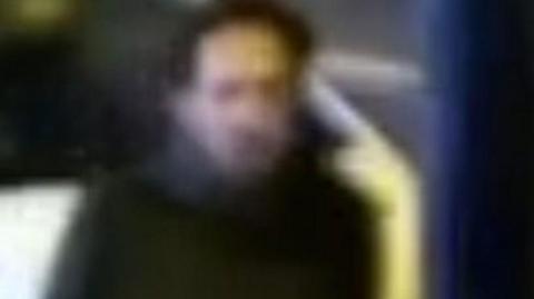 A CCTV image of a man police want to speak to. It is an unclear image which shows a man with dark hair wearing a dark coat. 