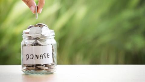 A person droping a coin into a donation hjar