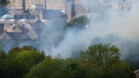 A view of smoke from behind trees in front of the backdrop of Matlock