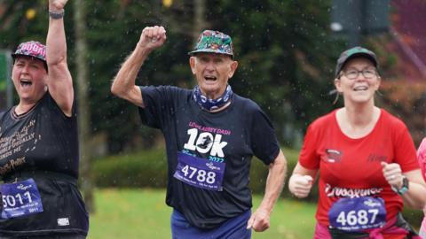 Two women and a man all wearing baseball caps and race numbers on their tops running in the rain