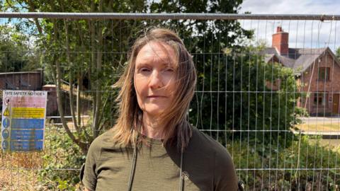 Collette Brown standing in her garden in Ansty, Warwickshire, in front of a safety fance and safety notice signs near a landslip.