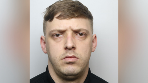 A man's police custody image. He has brown hair and short facial hair.