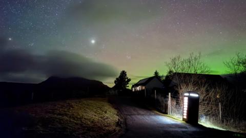 image of the night sky with hint of a green aurora and bright starts in the sky.  Two brighter lights shine which are Venus and Mars.