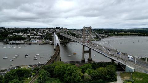 A drone picture of the Tamar Bridge taken from a distance. It shows the main bridge and the railway bridge with the town of Saltash in the background. 