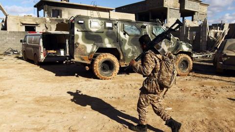 A member of the Libyan National Army (LNA) walks past an armoured vehicle as he holds a position during fighting against jihadists in Qanfudah, on the southern outskirts of Benghazi,