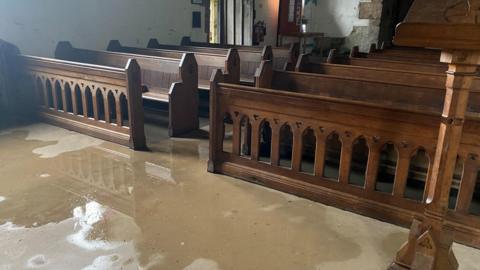 The inside of a church with wooden pews and water on the floor 