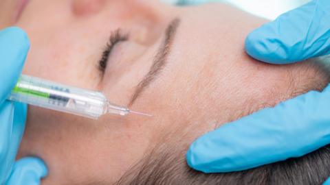 Stock image of a medical practitioner injecting using a needle into someone's forehead