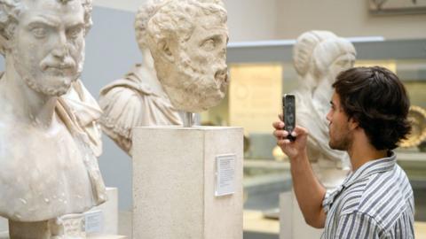 A visitor to the British Museum takes a photograph of a selection of Greek marble busts on August 23, 2023