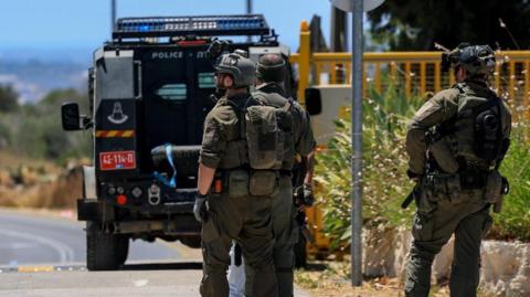 Three Israeli emergency personnel at the scene of the shooting with a police truck in front of them