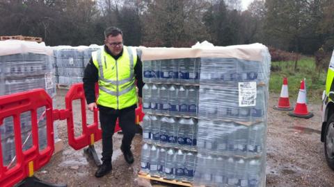 A man in hi vis jacket standing in a car park with a lot of bottles of water
