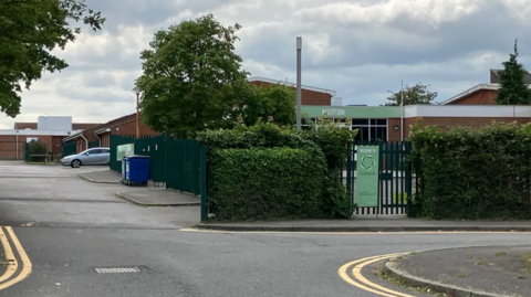 A general view picture of the school's site from a road outside it, including a green sign that says "Welcome to Oakbank".