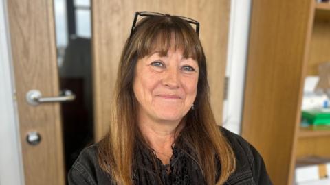 Sandy Denning, a woman with brown hair and a fringe looks stoically at the camera.