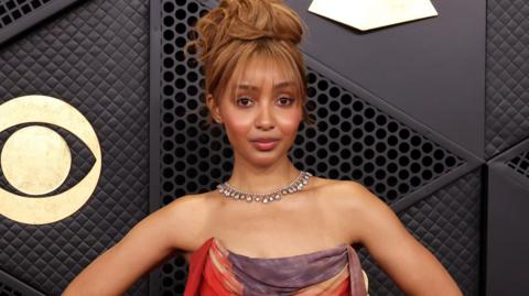 PinkPantheress posing on the Grammy Awards red carpet with a strapless red and grey dress and hair in a bun