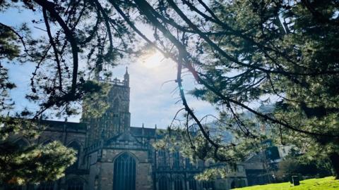 A large church and graveyard with blue sky and sunshine behind