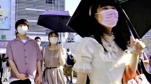 Pedestrians wearing face masks walk across the Shinjyuku shopping street in Tokyo on 28 July 2021