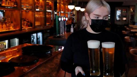 A bar worker serves pints of beer while wearing a mask