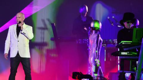 The Pet Shop Boys on stage performing with pink and purple lighting.