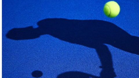 A blue padel court with a shadow of a person holding a racket 