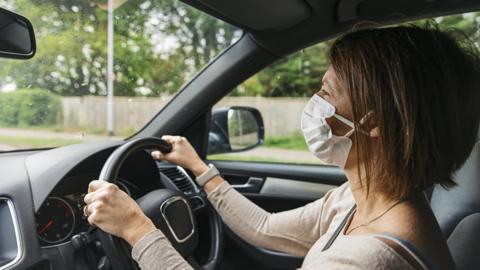 A woman driving a car in a mask