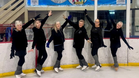 Group of iceskaters pose for a photograph on an ice rink.