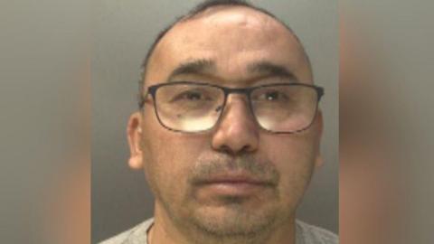 A mug shot of a man with dark hair and glasses