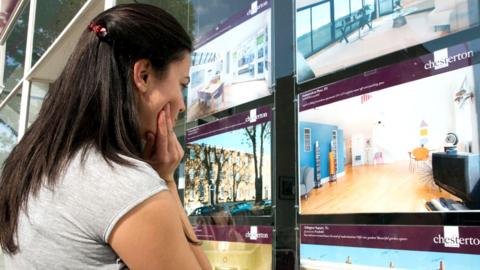 A young woman looking at adverts in an estate agents window