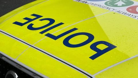 The fluorescent yellow bonnet of a police car, with the word police in reverse letters.