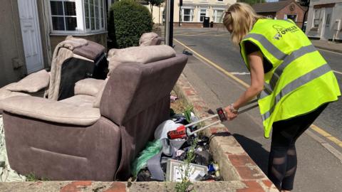 Tony Preston, one of the Wombles in Spalding, is dressed in a high visibility jacket and is seeing picking litter beside a couple of dumped sofas