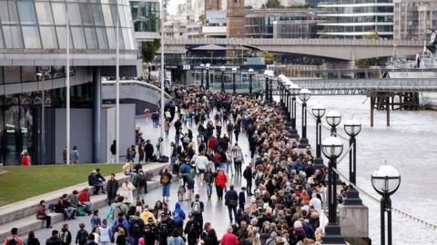 People queue on The Queen's Walk along the River Thames