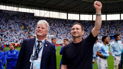 Coventry City owner Doug King pictured with manager Frank Lampard at the Coventry Building Society Arena celebrating with fans. They are both smiling and Frank Lampard has his left first raised in celebration.