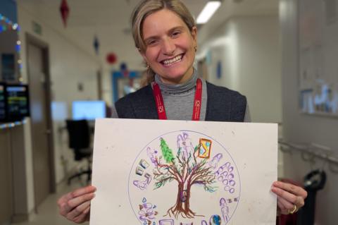 Dr Lani Walshaw, a woman with blonde hair, smiling at the camera as she holds up her artwork