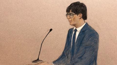 A court sketch of the defendant, who is sitting in the dock, wearing a blue suit with a white shirt and blue tie. He has short black hair and is wearing glasses.  