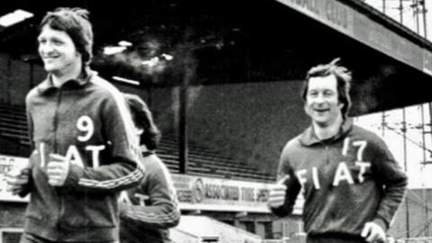 A black and white photo of three Cambridge United players wearing tracksuits saying Fiat running at the Abbey Stadium in about the late 1970s or 1980s