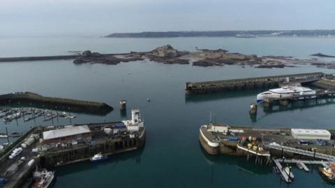 Jersey's ferry port on an overcast day. There are boats moored in the harbour and a ferry in the dock.