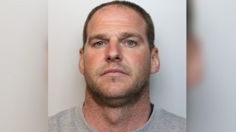 Police mugshot of Shaun Bundy. He has a short, stubbly beard, short hair and is wearing a grey top. 