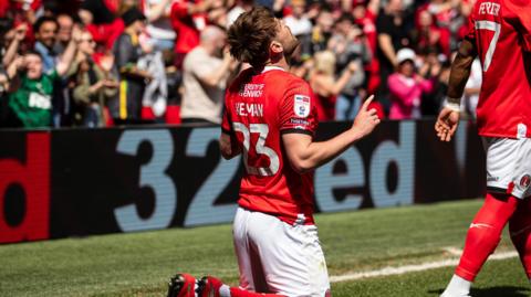 Charlie Kelman kneels on the turf and raises his arms aloft, looking up to the sky