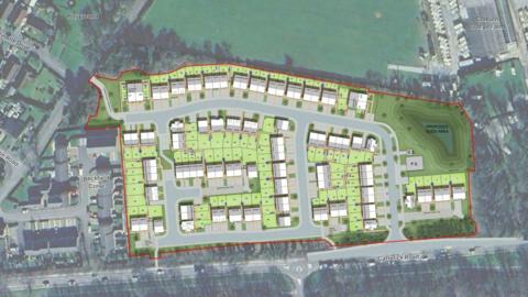 A birdseye view of a proposed development. The rooves of dozens of houses are pictured within a red boundary line, complemented by green space.
