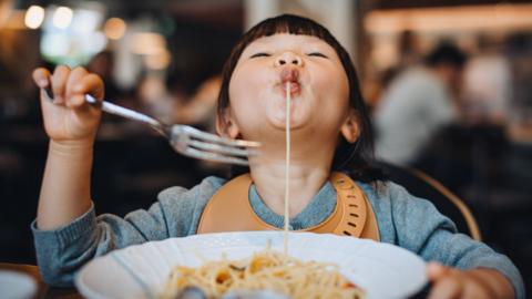 A child eats a plate full of spaghetti up in a restaurant.
