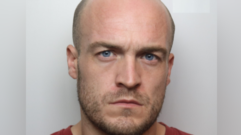 A custody image of Bradley Nightingale, who has a shaved head and a light beard. He is wearing a red T-shirt.
