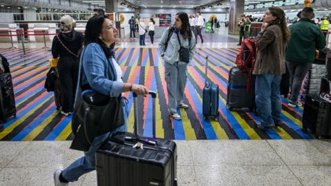 People queue to check in, with one person at the front wheeling a suitcase, at Simon Bolivar International Airport in Maiquetia, near Caracas, Venezuela, 26 November 2025