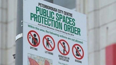 A white sign showing actions that are banned in the area of the PSPO, such as spitting, littering, urinating and defecating and begging. The sign has written in green "Peterborough City Centre Public Spaces Protection Order". 