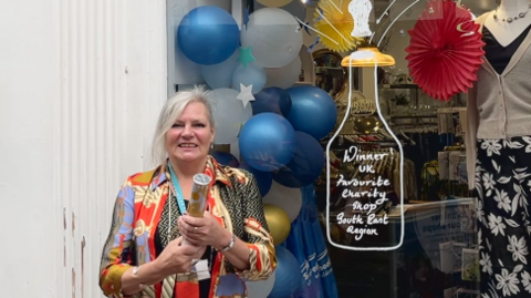 Branch manager Julie Bunting holds a streamer in front of her standing in front of the shop window with decorations and clothes seen in the background