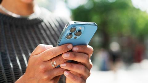 A close up of a person's hands holding a blue iphone, which we can only see the back of.