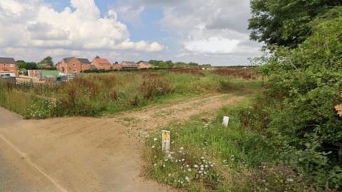 The site of 35 proposed houses on Station Road, Digby. There is a farm track leading into a field in the foreground, and behind the field are new-build houses and construction items.