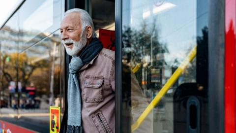A senior man gets off a red bus.