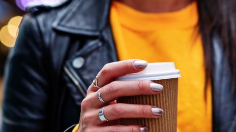 A woman in a leather jacket holding a takeaway coffee cup