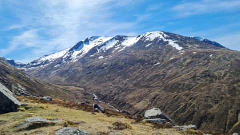 Photograph of a mountain with snow on the peaks along with sunny spells
