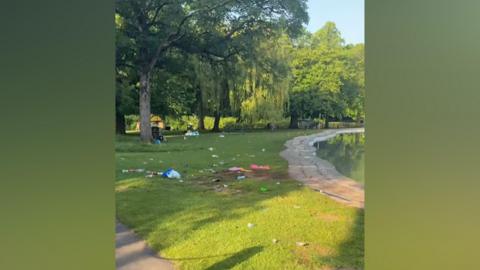 Litter sprawled across a stretch of green in a park near a paddling pool.
